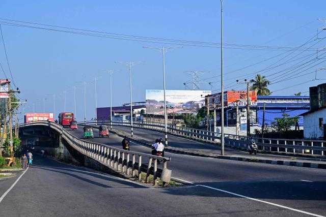 Commuters ride along a deserted street in Colombo on March 25, 2026 after Sri Lanka introduced a four-day work week to conserve fuel reserves amid the Middle East war. Sri Lanka ordered street lights, neon signs and billboard lighting to be switched off from March 24 as part of measures to cut energy consumption by 25 percent to tackle supply shortages. The island brought back work-from-home arrangements since last week, to reduce pressure on the transport network. (Photo by Ishara S. KODIKARA / AFP)