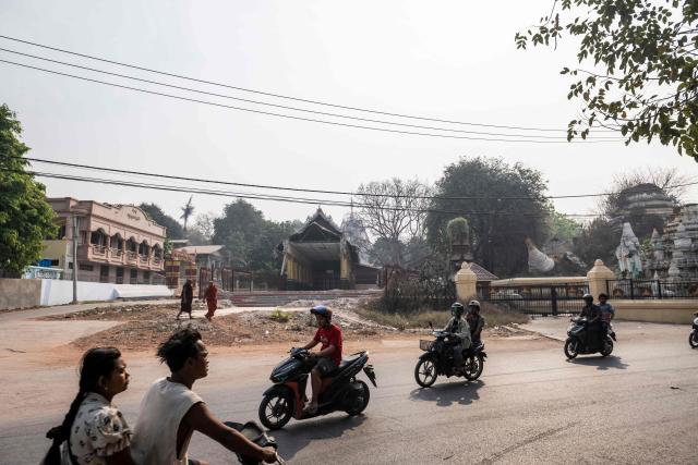 This photo taken on March 19, 2026 shows people commuting past the cleared site of a pagoda in Mandalay that was damaged during a magnitude 7.7 magnitude earthquake on March 28, 2025. The magnitude 7.7 magnitude earthquake on March 28, 2025 killed more than 3,700 people as it razed buildings in Myanmar's central belt, with devastation focused on the second-most-populous city of Mandalay. (Photo by Sai Aung MAIN / AFP)