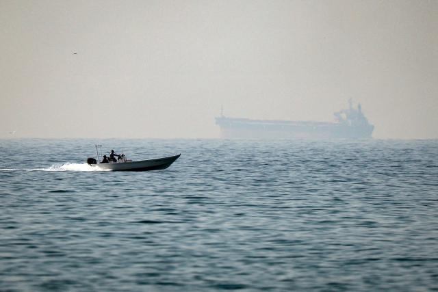 (FILES) A motorboat cruises along the shore off the town of Al Jeer on the Strait of Hormuz in the northern emirate of Ras Al Khaimah, with a tanker seen in the background, on February 25, 2026. The US president sent a peace plan to Iran as he voiced optimism on March 25, 2026 at ending nearly a month of warfare, with Tehran announcing that it will let "non-hostile" oil vessels go through the crucial Strait of Hormuz. Oil prices dropped sharply and stocks in Asia rose on broader de-escalation hopes following nearly four weeks of war, as the US president appeared to be ramping up efforts to bring an end to his joint military operation with Israel. (Photo by FADEL SENNA / AFP)