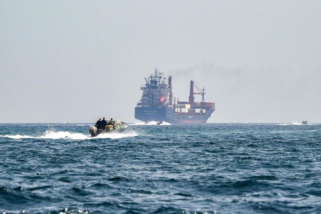 (FILES) A boat approaches the St Kitt's and Nevis-flagged container ship Marsa Victory while crusing in the waters of the Strait of Hormuz off the coast of Khasab in Oman’s northern Musandam peninsula on June 25, 2025. Oil prices dropped sharply and stocks in Asia rose on broader de-escalation hopes following nearly four weeks of war, as the US president appeared to be ramping up efforts to bring an end to his joint military operation with Israel on March 25, 2026. (Photo by Giuseppe CACACE / AFP)