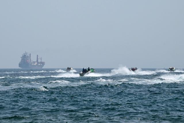(FILES) Small boats loaded with merchandise sail past the St Kitt's and Nevis-flagged container ship Marsa Victory in the waters of the Strait of Hormuz off the coast of Khasab in Omans northern Musandam peninsula on June 25, 2025. The US president sent a peace plan to Iran as he voiced optimism on March 25, 2026 at ending nearly a month of warfare, with Tehran announcing that it will let "non-hostile" oil vessels go through the crucial Strait of Hormuz. Oil prices dropped sharply and stocks in Asia rose on broader de-escalation hopes following nearly four weeks of war, as the US president appeared to be ramping up efforts to bring an end to his joint military operation with Israel. (Photo by Giuseppe CACACE / AFP)