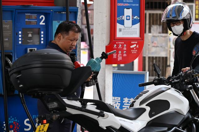 A pump attendant (L) fills up a motorcycle at a petrol station in Hong Kong on March 25, 2026. (Photo by Peter PARKS / AFP)