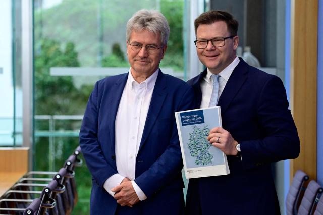 German Minister for the Environment, Climate Protection, Nature Conservation and Nuclear Safety Carsten Schneider poses with the government's report: "Program for Climate Protection 2026" next to the Head of the Department for National and European Climate Action Berthold Goeke at the BPK (Bundespressekonferenz) building in Berlin, on March 25, 2026. (Photo by John MACDOUGALL / AFP)