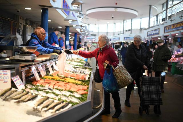 A shopper (C) buys fresh items at one of the stalls at Bury Market in Bury, Greater Manchester on March 25, 2026. Britain's annual inflation rate was unchanged at 3.0 percent in February, official data showed on March 25 ahead of an expected jump as the Middle East war has sent oil prices surging. (Photo by Oli SCARFF / AFP)
