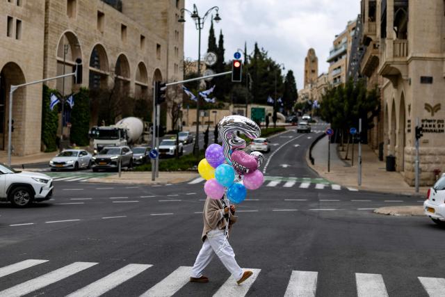 A woman carrying birthday balloons crosses a road in West Jerusalem, on March 25, 2026.  (Photo by Odd ANDERSEN / AFP)