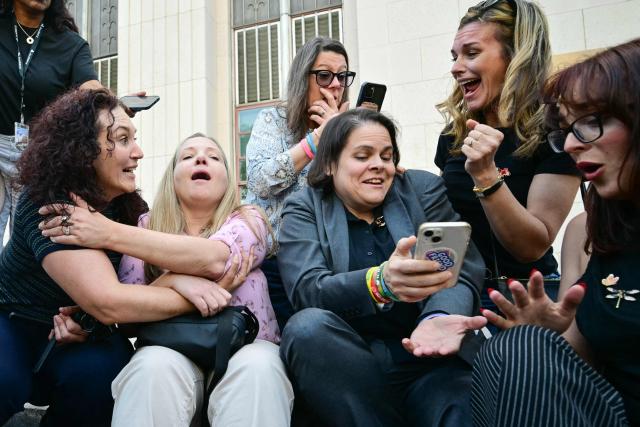 TOPSHOT - Laura Marquez-Garrett (3R, gray blazer), plaintiffs' attorney for SMVLC (Social Media Victims Law Center), gathers with family members of victims as they react to news that the jury has found Meta and YouTube liable in the social media addiction trial, outside the Los Angeles Superior Court , in Los Angeles, on March 25, 2026. (Photo by Frederic J. Brown / AFP)