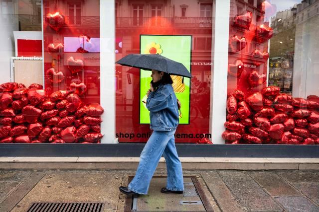 A pedestrian walks past a shop window decorated with heart-shaped balloons in a rainy day in central Paris on March 25, 2026. (Photo by Blanca CRUZ / AFP)