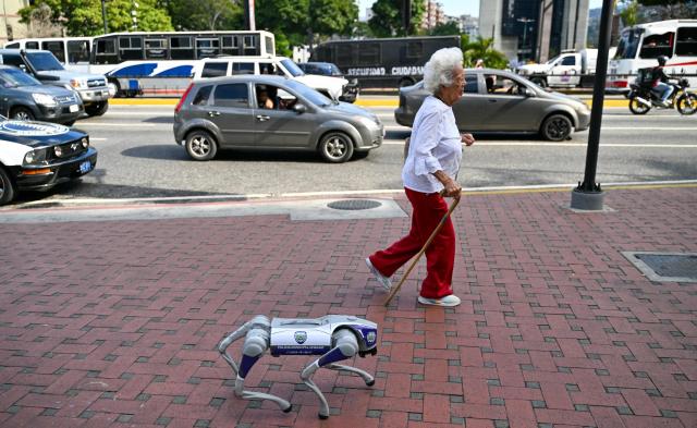 A woman walks next to a robot dog of the Chacao municipal police in a square in Caracas on March 25, 2026. (Photo by Juan BARRETO / AFP)