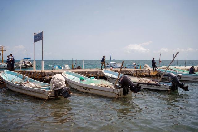 Members of the Navy stand on a pier next to small fishing boats in Boca del Rio, Veracruz state, Mexico, on March 25, 2026. The Mexican government said on March 25 that it has removed 128 tons of crude oil residue from the Gulf of Mexico following a spill first reported in early March. (Photo by Victoria Razo / AFP)