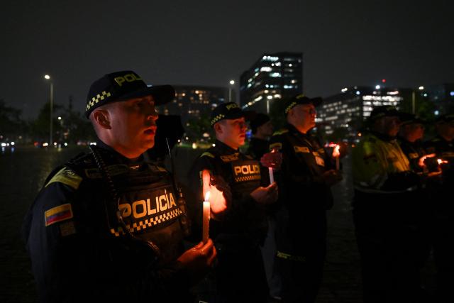 Colombian police officers hold candles during vigil for the victims of the Colombian Air Force Hercules crash in Puerto Leguizamo, in Bogota on March 25, 2026. At least 69 soldiers and police officers were killed in one of the deadliest air accidents in Colombia's recent history, according to a new March 24 tally of the crash, which the government attributed to a ‘junk’ aircraft donated by the United States. (Photo by Daniel MUNOZ / AFP)