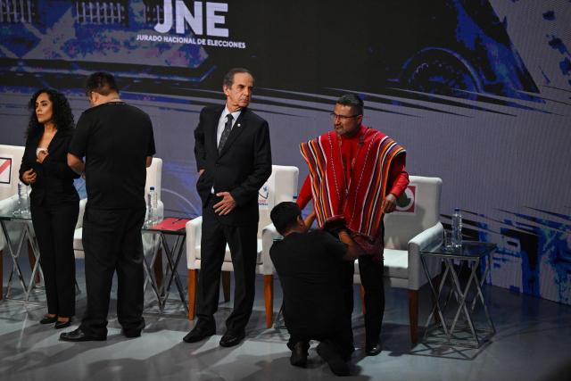 (L-R) Sound technicians wire up Peru's presidential candidates Rosario Fernandez, for the Un Camino Diferente party; Roberto Chiabra, for the National Unity party; and Ronald Atencio, for the Venceremos electoral alliance; ahead of the third round of debates on tackling crime and corruption at the Lima Convention Center in Lima on March 25, 2026. Peru will hold presidential elections on April 12. (Photo by ERNESTO BENAVIDES / AFP)