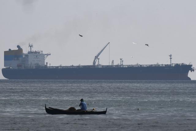 A fisherman paddles before the Sierra Leone-flagged Sara Sky, which is carrying crude oil from Russia, anchored at Limay port, Bataan province on March 26, 2026. (Photo by Ted ALJIBE / AFP)