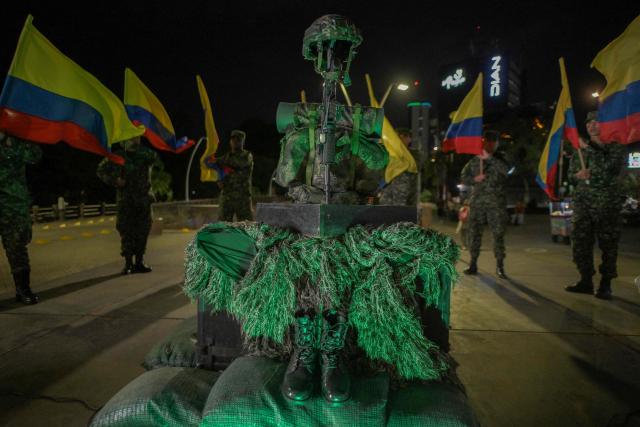 Colombian soldiers hold Colombian flags around a monument prepared for a vigil for the victims of the Colombian Air Force Hercules crash in Puerto Leguнzamo, outside La Ermita church in Cali, Colombia, on March 25, 2026. At least 69 soldiers and police officers were killed in one of the deadliest air accidents in Colombia's recent history, according to a new March 24 tally of the crash, which the government attributed to a ‘junk’ aircraft donated by the United States. (Photo by Joaquнn SARMIENTO / AFP)