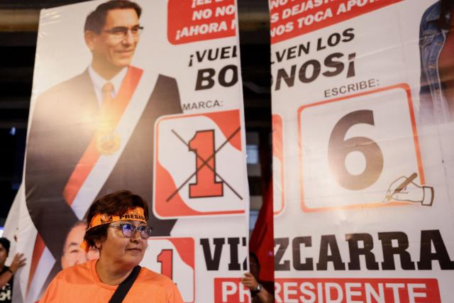 A supporter of Peru's presidential candidate Keiko Fujimori, for the Fuerza Popular party, stands in front of a banner depicting presidential candidate Mario Vizcarra, for the First Peru party, during the third round of debates on tackling crime and corruption at the Lima Convention Center in Lima on March 25, 2026. Peru will hold presidential elections on April 12. (Photo by Connie FRANCE / AFP)