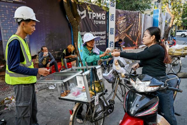 A woman (R) buys cake from a vendor on a street in Phnom Penh on March 26, 2026. (Photo by TANG CHHIN Sothy / AFP)