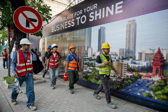 Construction workers walk past a billboard on a street in Phnom Penh on March 26, 2026. (Photo by TANG CHHIN Sothy / AFP)