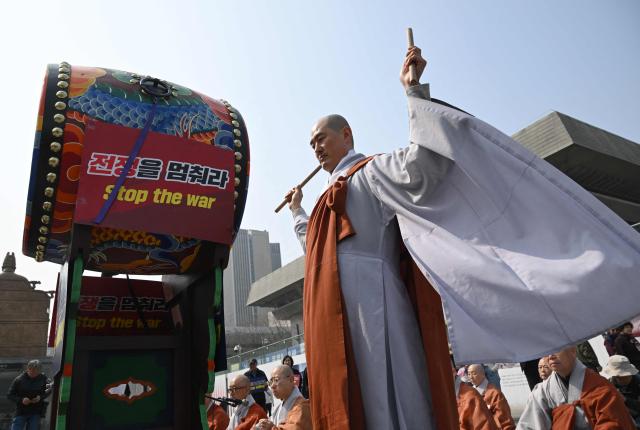A South Korean Buddhist monk beats a ceremonial drum with a sign reading "Stop the war" during a prayer service opposing the war on Iran in front of the US embassy in Seoul on March 26, 2026. (Photo by Jung Yeon-je / AFP)