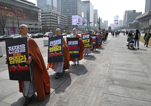 South Korean Buddhist monks carry placards reading "Stop the war" as they march during a prayer service opposing the war on Iran at Gwanghwamun Square near the US embassy in Seoul on March 26, 2026. (Photo by Jung Yeon-je / AFP)