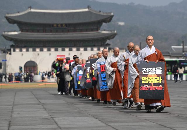 South Korean Buddhist monks carry placards reading "Stop the war" as they march during a prayer service opposing the war on Iran at Gwanghwamun Square near the US embassy in Seoul on March 26, 2026. (Photo by Jung Yeon-je / AFP)
