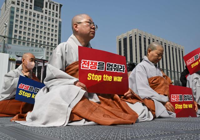 South Korean Buddhist monks hold signs reading "Stop the war" during a prayer service opposing the war on Iran in front of the US embassy in Seoul on March 26, 2026. (Photo by Jung Yeon-je / AFP)