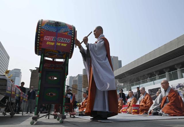 A South Korean Buddhist monk beats a ceremonial drum with a sign reading "Stop the war" during a prayer service opposing the war on Iran in front of the US embassy in Seoul on March 26, 2026. (Photo by Jung Yeon-je / AFP)