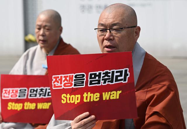 South Korean Buddhist monks hold signs reading "Stop the war" during a prayer service opposing the war on Iran in front of the US embassy in Seoul on March 26, 2026. (Photo by Jung Yeon-je / AFP)