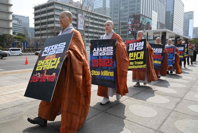 South Korean Buddhist monks carry placards reading "Stop the war" as they march during a prayer service opposing the war on Iran at Gwanghwamun Square near the US embassy in Seoul on March 26, 2026. (Photo by Jung Yeon-je / AFP)