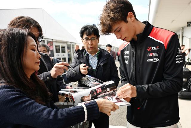 Haas F1 Team's British driver Oliver Bearman (R) gives his autograph to fans preparing for the March 29 Formula One Japanese Grand Prix race at the Suzuka circuit in Suzuka, Mie prefecture on March 26, 2026. (Photo by Toshifumi KITAMURA / AFP)