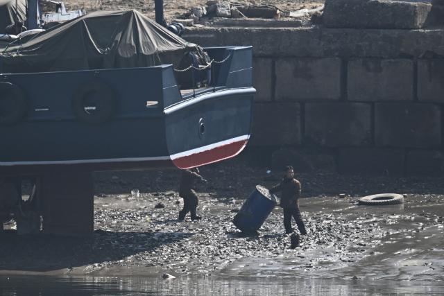 North Korean men are seen next to a boat in the North Korean town of Sinuiju, opposite the border city of Dandong, in China's northeast Liaoning province on March 26, 2026. Passenger rail travel between China and North Korea resumed on March 12, after a pause of more than six years triggered by the COVID-19 outbreak. (Photo by GREG BAKER / AFP)