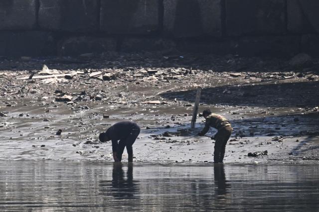 North Korean men are seen on the bank of the Yalu River in the North Korean town of Sinuiju, opposite the border city of Dandong, in China's northeast Liaoning province on March 26, 2026. Passenger rail travel between China and North Korea resumed on March 12, after a pause of more than six years triggered by the COVID-19 outbreak. (Photo by GREG BAKER / AFP)