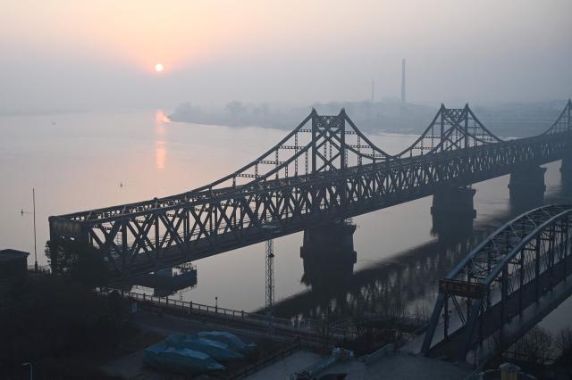 The sun rises over the North Korean town of Sinuiju, behind the Sino-Korean Friendship Bridge (L) and the Yalu River Broken Bridge (R), as seen from the border city of Dandong, in China's northeast Liaoning province on March 26, 2026. Passenger rail travel between China and North Korea resumed on March 12, after a pause of more than six years triggered by the COVID-19 outbreak. (Photo by GREG BAKER / AFP)