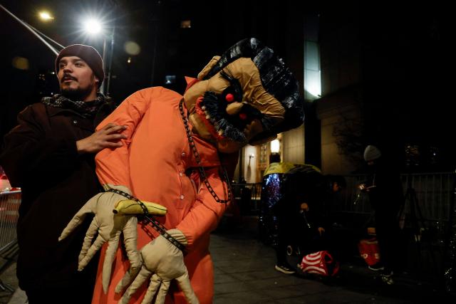 A man holds a makeshift inflatable figure of ousted Venezuelan president Nicolas Maduro handcuffed next to the Daniel Patrick Moynihan United States Courthouse as a convoy believed to be carrying Nicolas Maduro has arrived for his federal court appearance in Manhattan on March 26, 2026. Lawyers for the ousted Venezuelan president Nicolas Maduro are expected to push for the dismissal of his drug trafficking charges when he appears in a New York court March 26. The Manhattan hearing comes as Washington cautiously warms ties with Caracas, with the question of who will pay the legal fees of the former autocrat and his wife expected to take center stage. (Photo by John Lamparski / AFP)