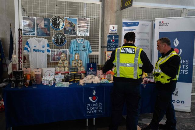 Marseille customs officers stand next to counterfeit goods seized at the port of Marseille during the presentation of the 2025 results by the Marseille customs directorate, in Marseille, on March, 26, 2026. (Photo by Elodie CLEMENT / AFP)