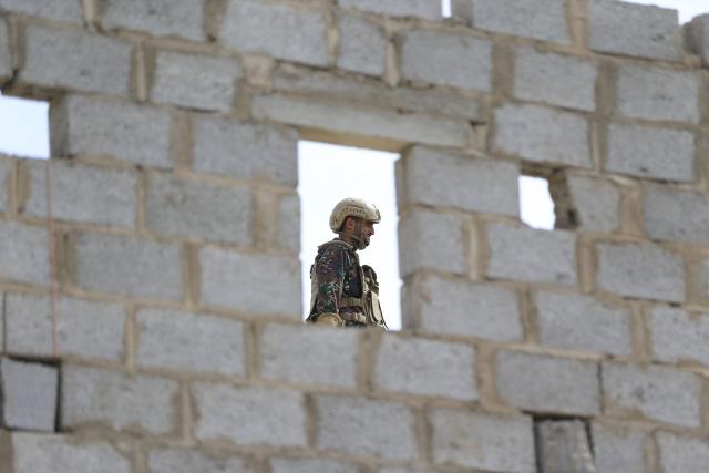 A Yemeni soldier stands guard on the roof of a building while supporters of Yemen's Huthi movement attend an event commemorating the ninth anniversary of the Saudi-led intervention in their country, in the capital Sanaa on March 26, 2026. (Photo by Mohammed HUWAIS / AFP)