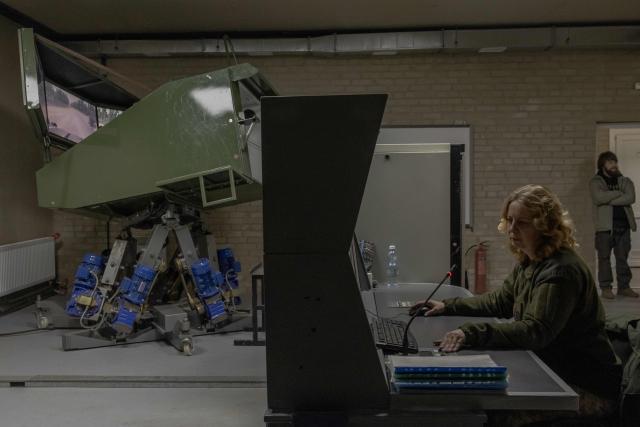 A Ukrainian military member looks at screens as a Ukrainian serviceman practices his driving skills on an armoured vehicle simulator at the Ukrainian Ground Forces training center in an undisclosed location on March 25, 2026, amid the Russian invasion of Ukraine. (Photo by Roman PILIPEY / AFP)