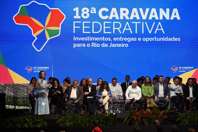 Brazil's Secretary of Institutional Affairs Gleisi Hoffmann (L) speaks as Brazil's President Luiz Inacio Lula da Silva (5-R) listens next to Brazil's Minister of Racial Equality Anielle Franco (4-R) during an event to announce investments as part of the Caravana Federativa program in Niteroi, Brazil, on March 26, 2026. (Photo by Mauro PIMENTEL / AFP)