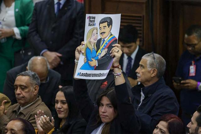 A deputy shows a sign depicting Venezuela's ousted president Nicolas Maduro and his wife Cilia Flores before a session at the National Assembly in Caracas on March 26, 2026. (Photo by Jesus VARGAS / AFP)