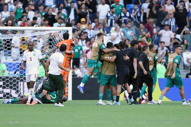 Bolivia's players and coaching staff celebrate their victory next to Suriname's defender #05 Dion Malone (L) during the 2026 FIFA World Cup qualifiers semi-final playoff football match between Bolivia and Suriname at the BBVA Stadium in Guadalupe, Mexico on March 26, 2026. (Photo by Julio Cesar AGUILAR / AFP)