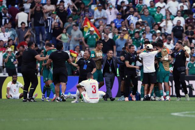 Bolivia's players and coaching staff celebrate their victory next to Suriname's defender #03 Radinio Balker during the 2026 FIFA World Cup qualifiers semi-final playoff football match between Bolivia and Suriname at the BBVA Stadium in Guadalupe, Mexico on March 26, 2026. (Photo by Julio Cesar AGUILAR / AFP)