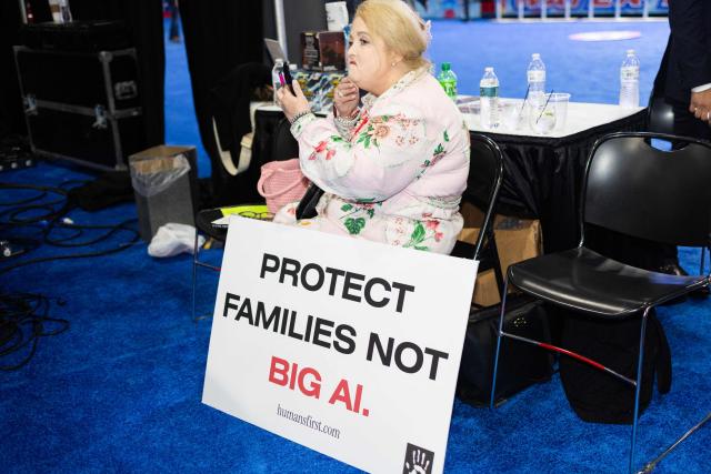 A woman adjusts her makeup while sitting with a sign expressing concerns about artificial intelligence at the Conservative Political Action Conference (CPAC) in Grapevine, Texas, on March 26, 2026. American conservatives converge on Texas this week for what organizers bill as their largest and most influential gathering, with the Iran war and fears of a punishing midterm election cycle heightening the stakes. (Photo by Leandro Lozada / AFP)
