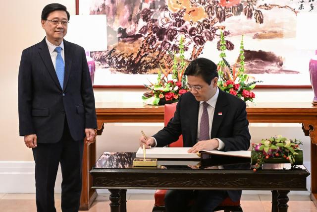Hong Kong Chief Executive John Lee (L) watches as Singapore's Prime Minister Lawrence Wong signs the visitors book at Government House in Hong Kong on March 27, 2026. (Photo by Peter PARKS / POOL / AFP)