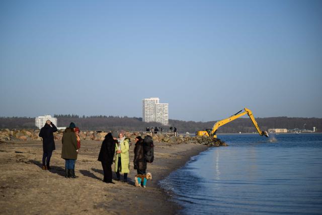 Onlookers stand on the beach in Niendorf, northern Germany, on March 27, 2026, with heavy machinery still visible in the background after a humpback whale that had run aground off the Baltic Sea coast apparently freed itself overnight following a large-scale rescue operation. The humpback whale that had been stranded for several days on Germany’s Baltic coast freed itself and was able to return to the sea, but still has a long way to go before it can reach its natural habitat, a scientist told the media on site. (Photo by DANIEL REINHARDT / AFP)