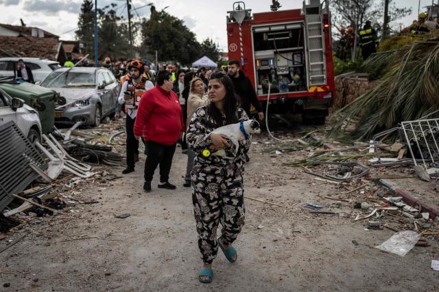 (FILES) A woman carries her pet dog as she leave the scene of a missile attack in Bet Shemesh, some 30 kilometres west of Jerusalem on March 1, 2026. The United States and Israel began the war on February 28, 2026, by attacking Iran and killing its supreme leader. Iran retaliated with strikes against Israel and US allies and interests across the Gulf and Iraq, drawing the whole region into war. (Photo by JOHN WESSELS / AFP)