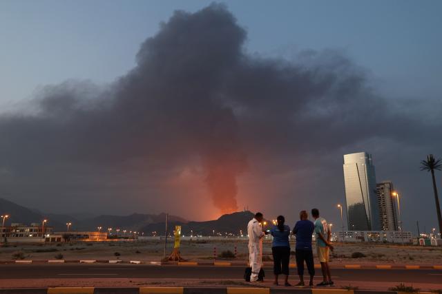 (FILES) Foreign workers look at a tall plume of black smoke ascends following an explosion in the Fujairah industrial zone on March 3, 2026. The United States and Israel began the war on February 28, 2026, by attacking Iran and killing its supreme leader. Iran retaliated with strikes against Israel and US allies and interests across the Gulf and Iraq, drawing the whole region into war. (Photo by Fadel SENNA / AFP)