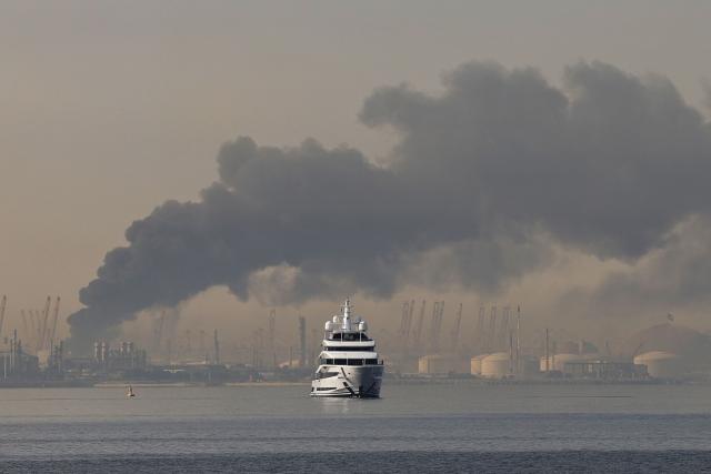 (FILES) A yacht sails past a plume of smoke rising from the port of Jebel Ali following a reported Iranian strike in Dubai on March 1, 2026. The United States and Israel began the war on February 28, 2026, by attacking Iran and killing its supreme leader. Iran retaliated with strikes against Israel and US allies and interests across the Gulf and Iraq, drawing the whole region into war. (Photo by Fadel SENNA / AFP)