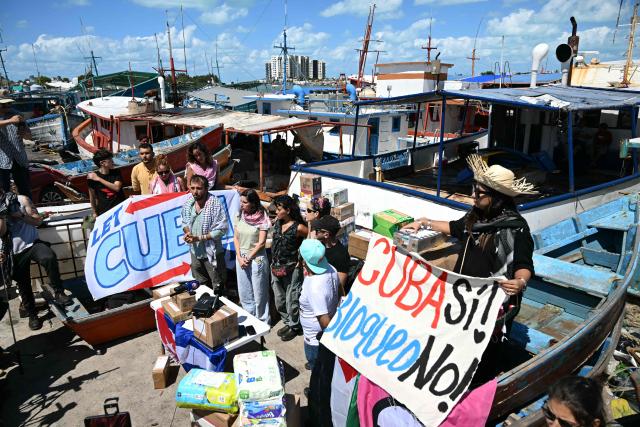(FILES) Activists hold a sign reading "Cuba Yes! Embargo No!" as a boat Maguro -- symbolically renamed "Granma 2.0" as a tribute to the yacht used by Fidel Castro's guerrilla fighters to launch their revolution in 1956 -- starts its journey to take humanitarian aid to Cuba, as part of the Convoy to Cuba, organised by left-wing activists from various countries in the Americas and Europe, in Puerto Progreso, Yucatan state, Mexico, on March 19, 2026. The Mexican Navy was searching on March 27 for two sailboats that went missing while transporting humanitarian aid to crisis-hit Cuba, a week after leaving Mexico. (Photo by YURI CORTEZ / AFP)