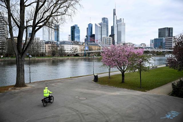 A person rides a bicycle along the banks of the Main river past a blossoming tree in Frankfurt am Main, western Germany, on March 27, 2026 as the air temperature reached 7 degrees Celsius above zero. (Photo by Kirill KUDRYAVTSEV / AFP)