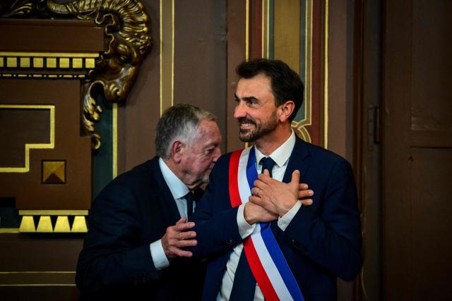 Newly re-elected Lyon mayor Gregory Doucet (R) reacts after receiving his mayoral sash from Jean-Michel Aulas (L), vice-president of the French Football Federation (FFF), during the inaugural session of the city council, central-eastern France, on March 27, 2026. (Photo by OLIVIER CHASSIGNOLE / AFP)