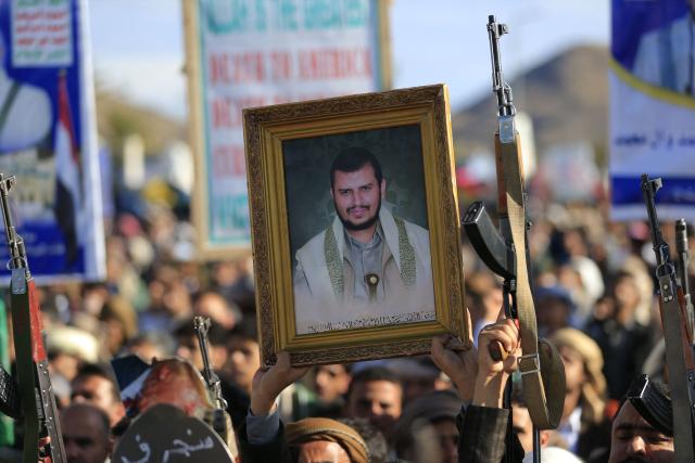 A supporter of Yemen's Huthis holds a picture of their leader Abdul-Malik al-Huthi as others brandish their weapons while rallying in solidarity with Iran and Lebanon, amid the US-Israeli war with Iran, in the Yemeni capital Sanaa on March 27, 2026. Abdul Malik al-Houthi, leader of Yemen's Iran-backed Houthi movement, warned on March 26 of a "military response" should the Middle East war require it. The Houthis, a key part of Iran's so-called "axis of resistance", have so far refrained from joining the war sparked by US-Israeli strikes on Iran, which has engulfed much of the region. (Photo by Mohammed HUWAIS / AFP)