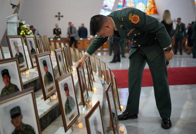 A uniformed service member places one of the portraits of the 69 soldiers and police officers who died in an Air Force Hercules accident during a religious ceremony in Bogota on March 27, 2026. The death toll in one of Colombia's worst air accidents in recent years rose to at least 69, according to an updated tally on March 24, as the government faulted a "junk" aircraft donated by the United States. (Photo by Sergio Yate / AFP)